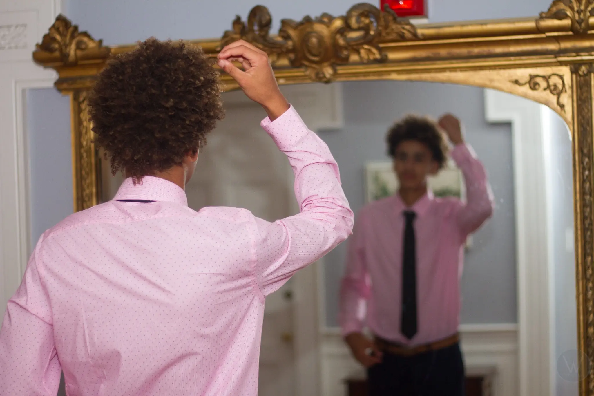 Wedding guest adjusting his hair in an ornate mirror